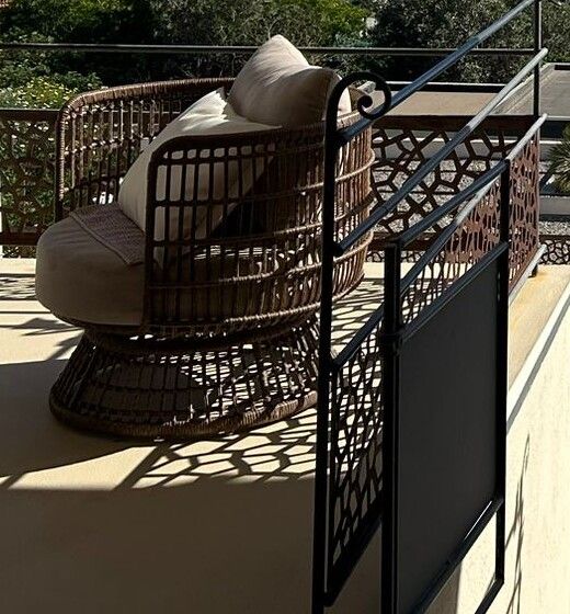 Le fauteuil en rotin et ses coussins, à l'ombre de la terrasse.