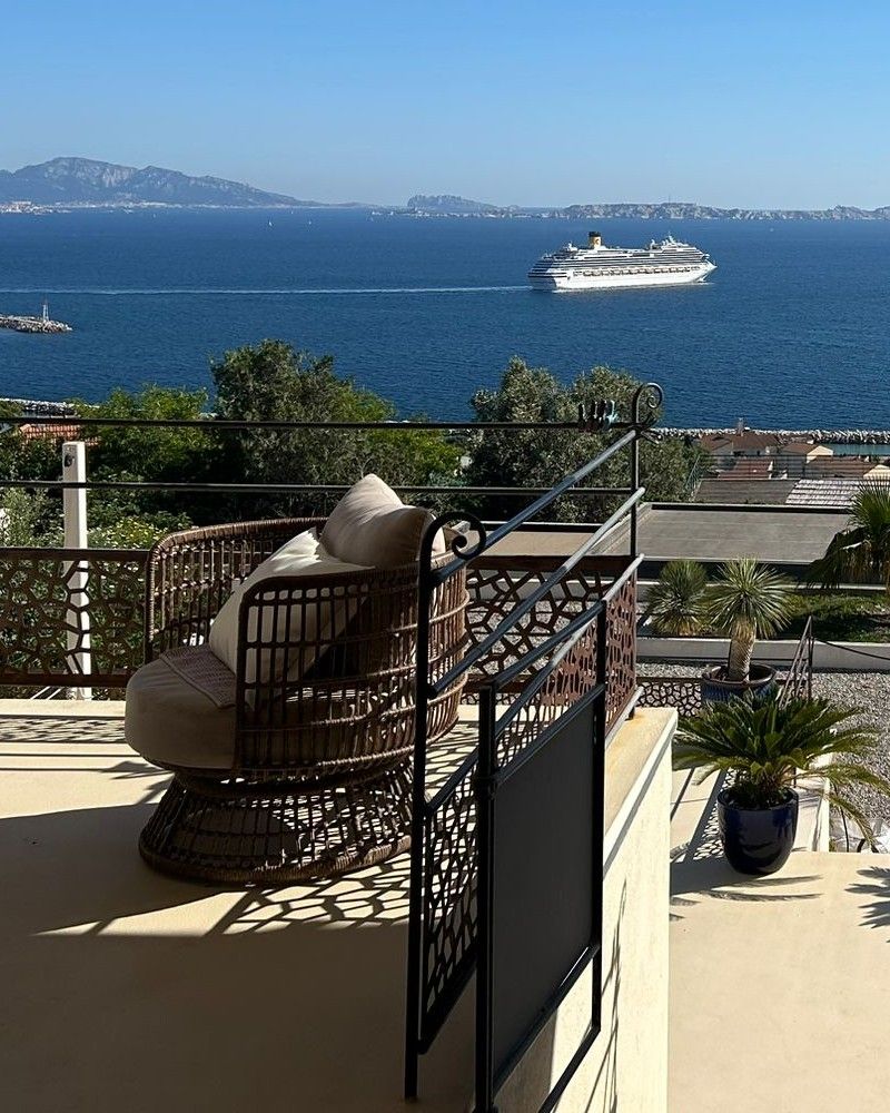 Un fauteuil en rotin sur la terrasse, face à la rade et à un paquebot.